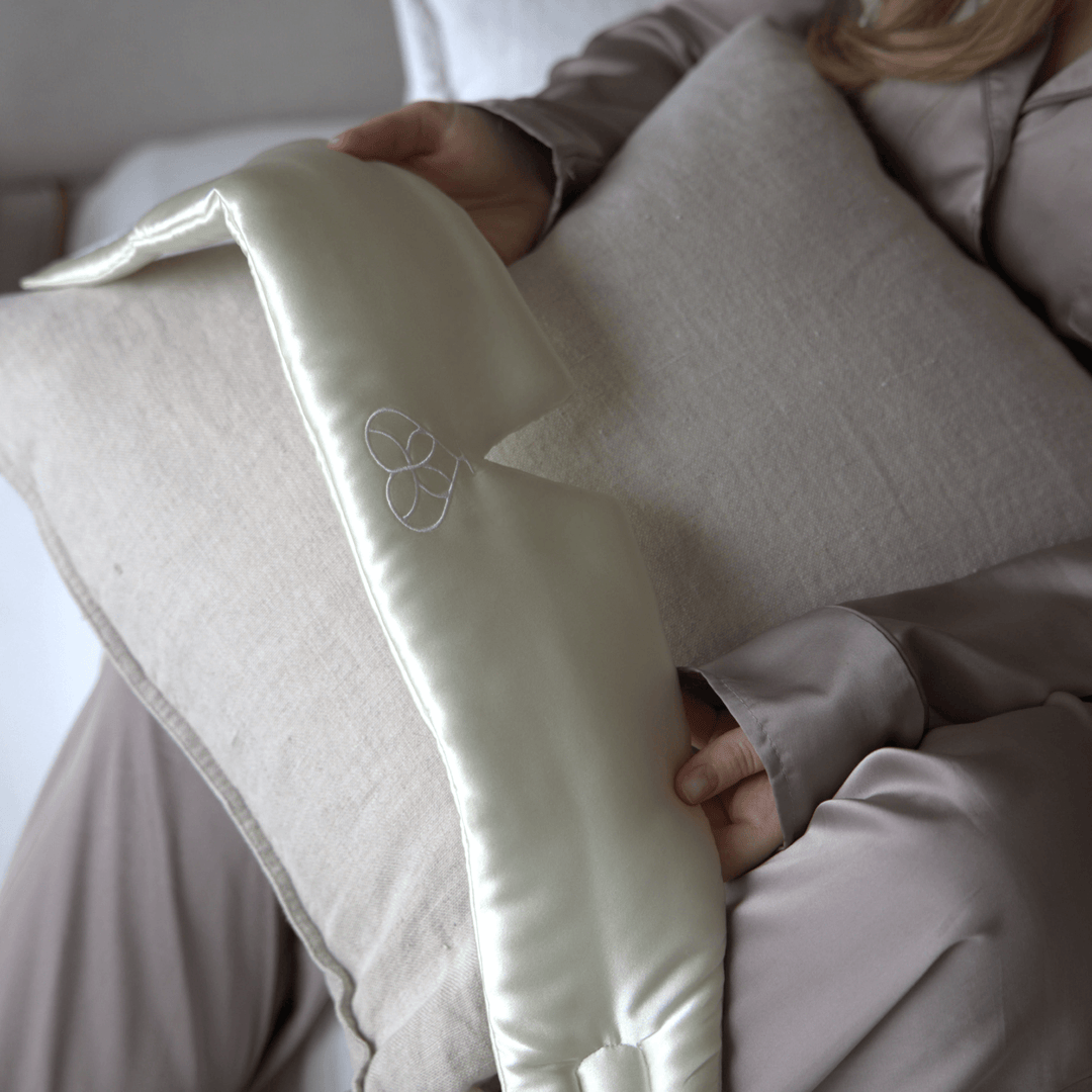 Masque de sommeil en soie crème tenu en main