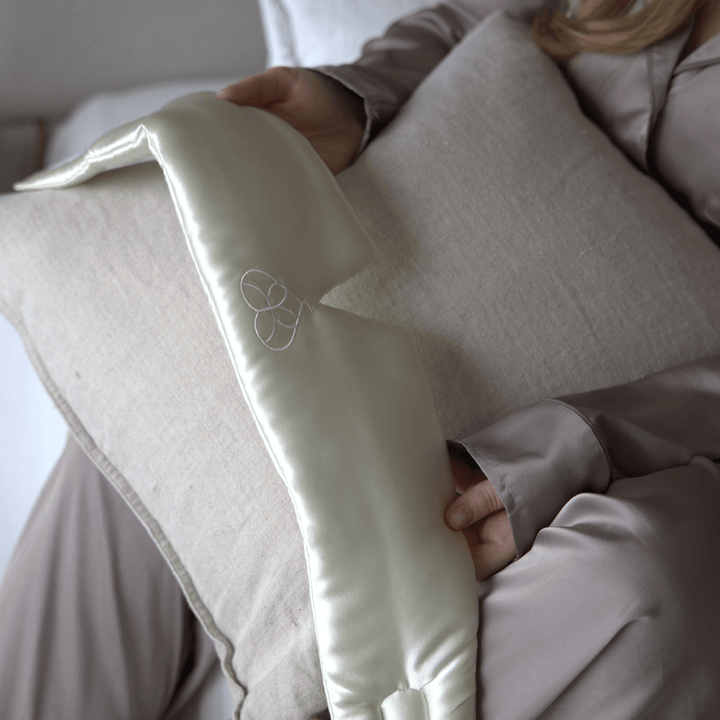 Masque de sommeil en soie crème tenu en main