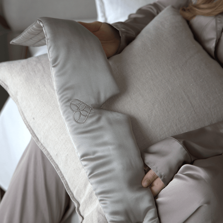 Masque de sommeil en soie gris tenu en main